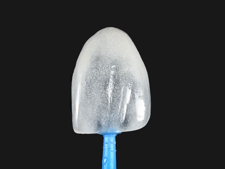 A single feldspathic veneer held on a blue microbrush